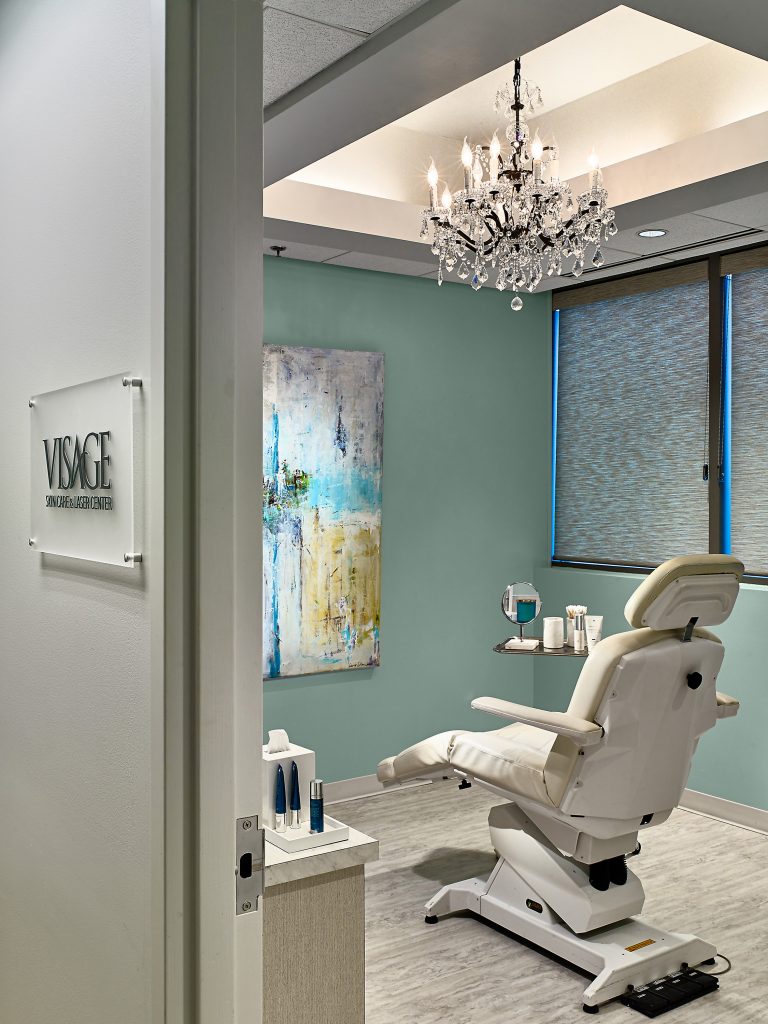 plastic surgery exam room with light teal walls and a glass chandelier hanging from the ceiling
