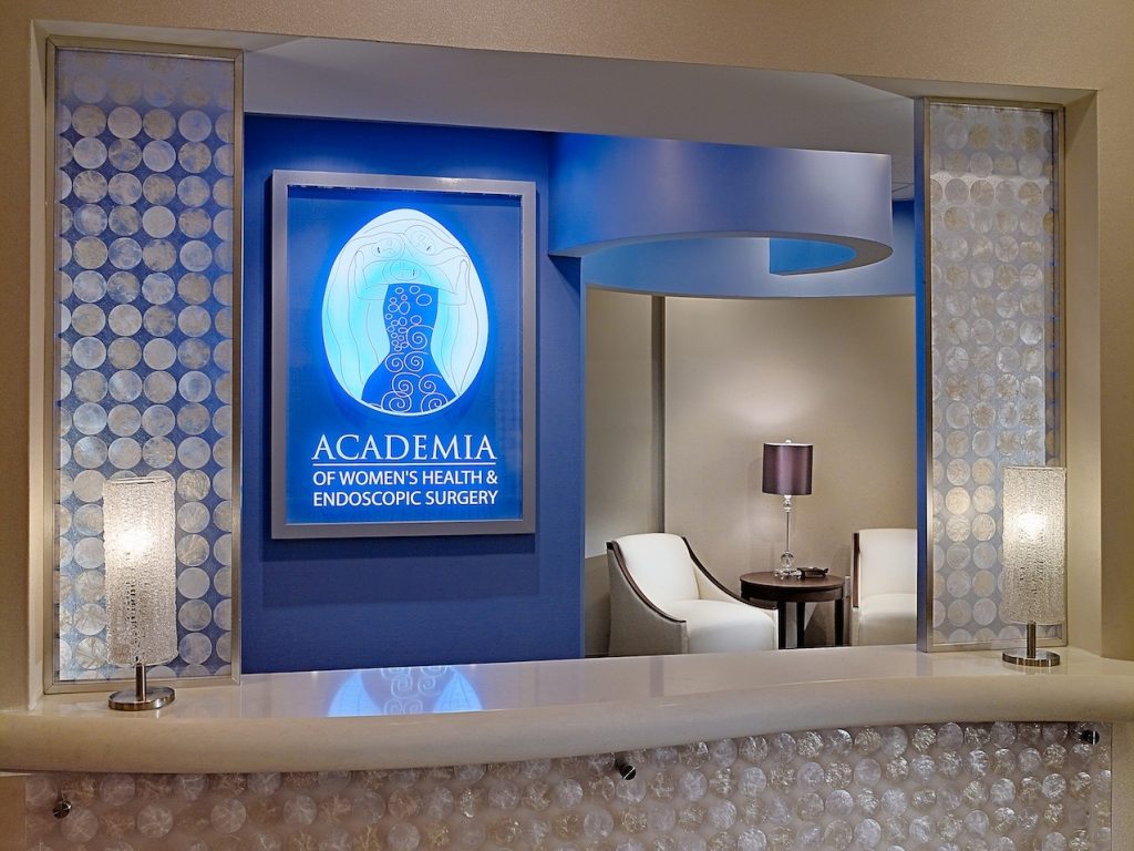 reception area at Academia of Women's Health with a glowing blue logo wall and decorative stone-covered counter