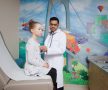 doctor examining a young girl with a stethoscope in front of a colorful bridge mural