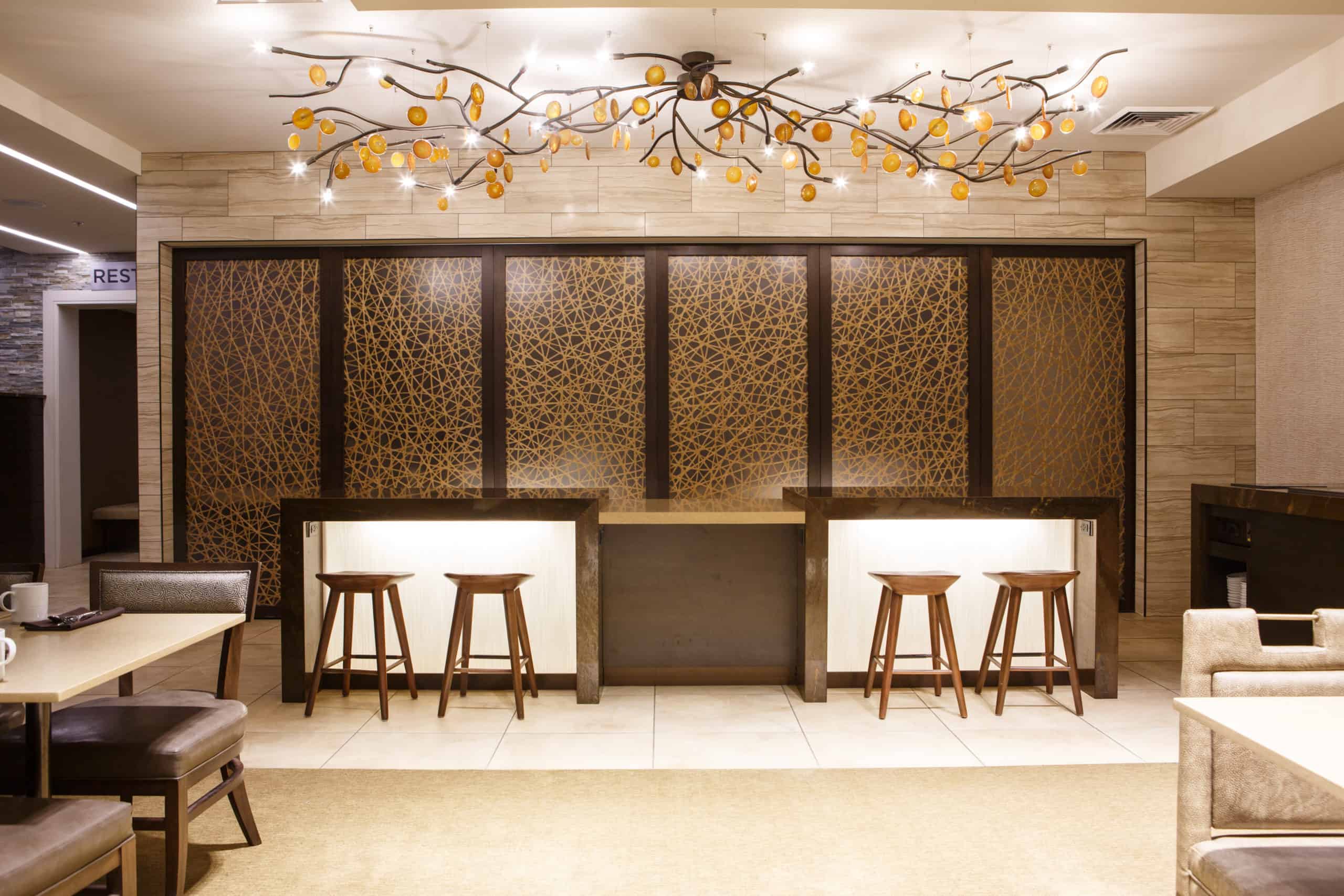 warmly lit cafe with barstools and a marble counter, sliding accent panels, and a large branching chandelier