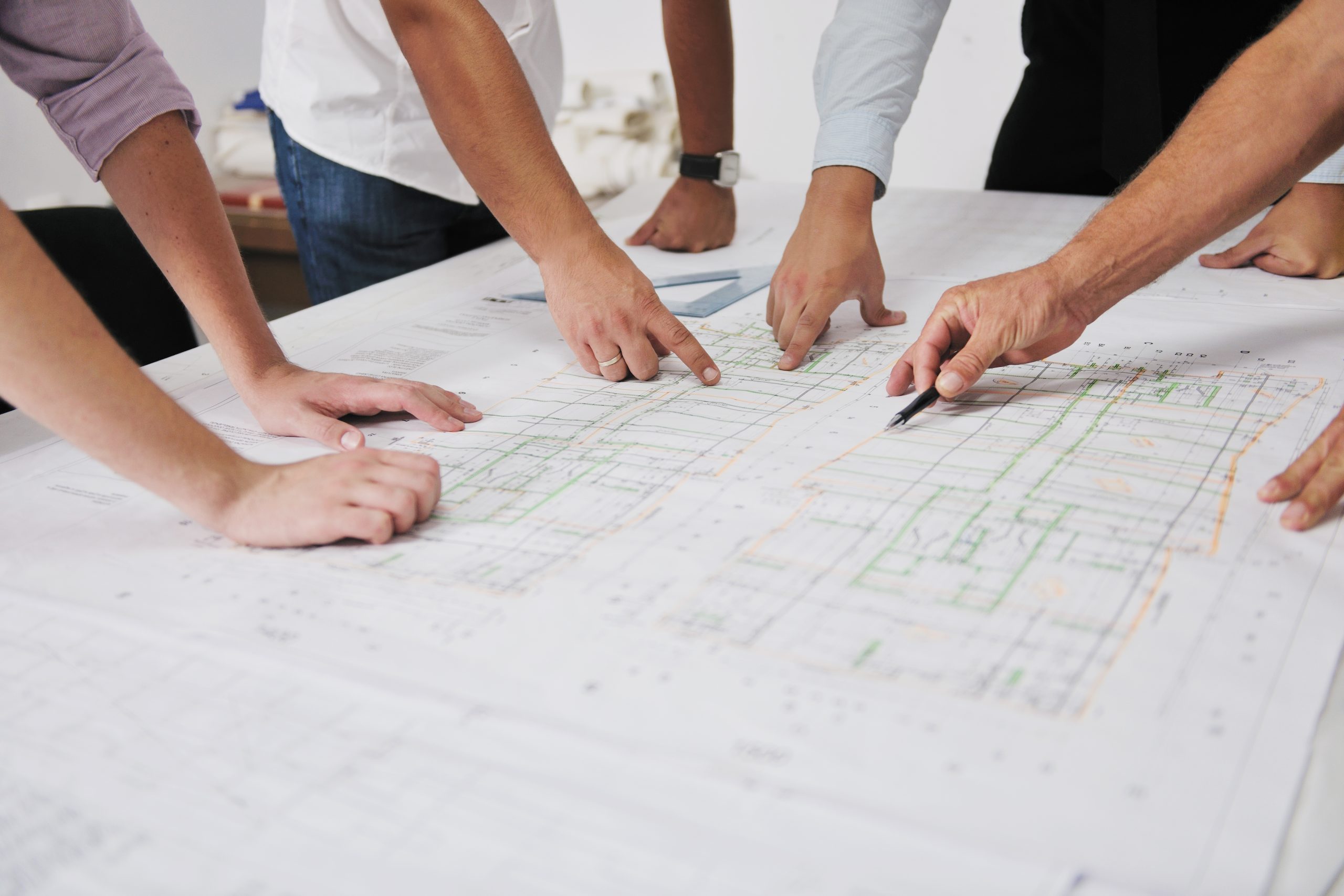 a group of people pointing at blueprint sheets